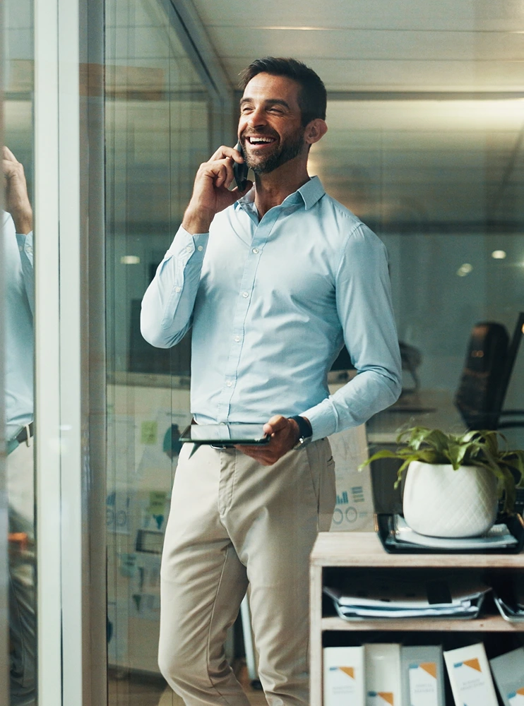 Smiling businessman on a phone call holding a tablet in an office