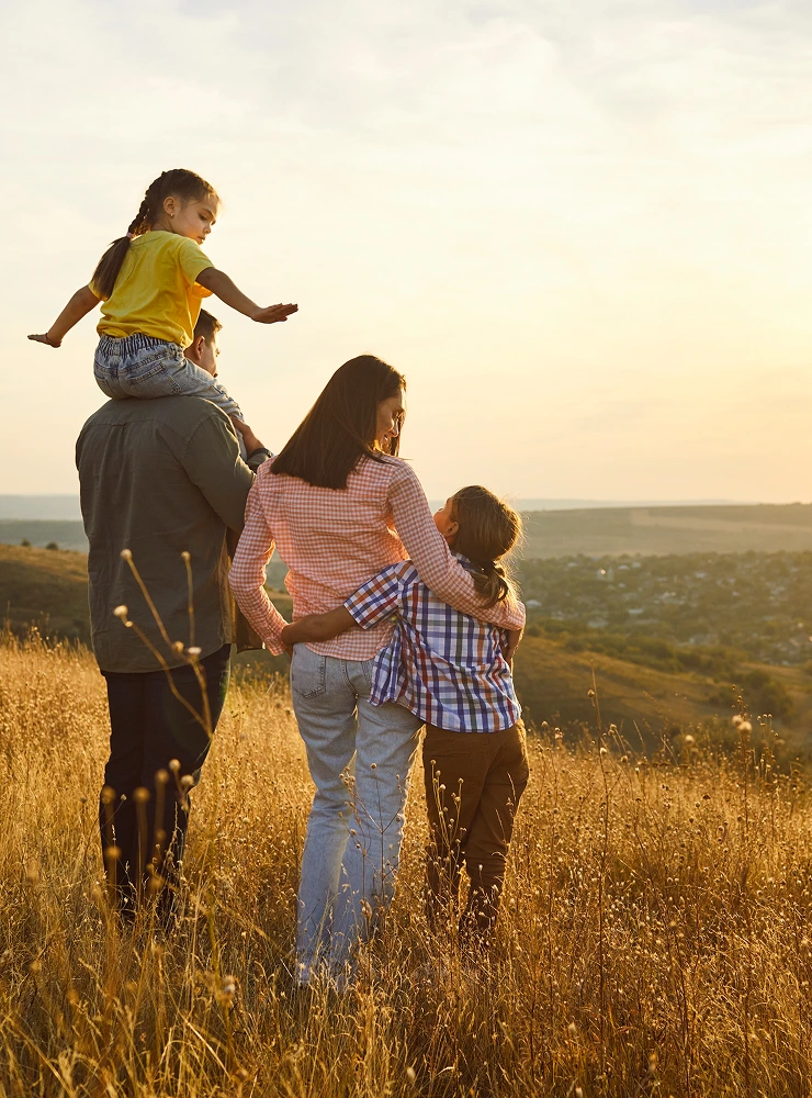Family walking hand in hand across a golden grassy hillside at sunset
