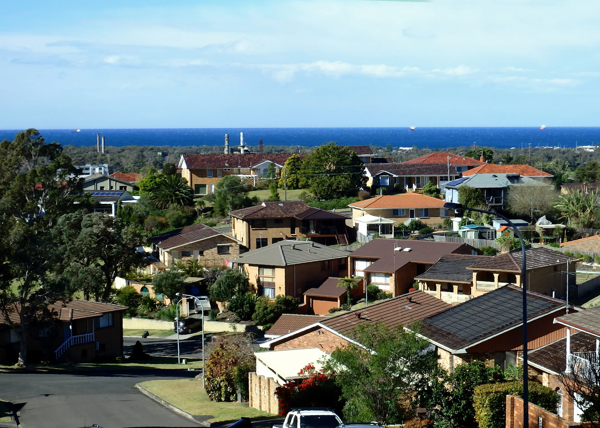 Elevated view of a coastal suburb with red-tile roofs and ocean