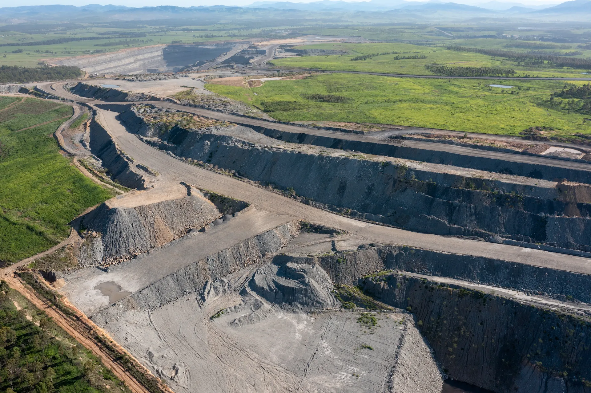 Aerial view of an open-cut mine pit beside green farmland